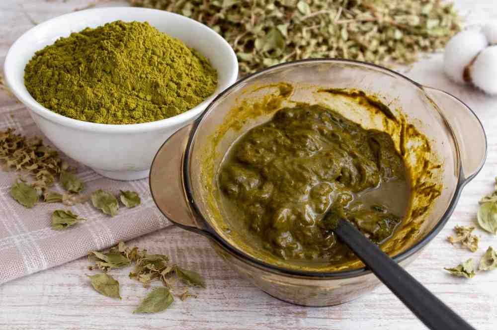 Henna powder in a bowl beside freshly mixed henna paste in a glass container with a spoon